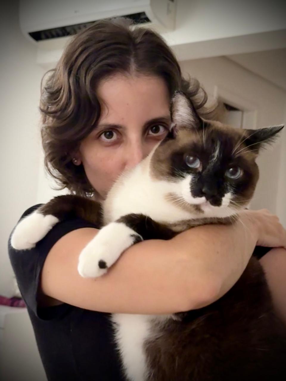 Amanda P. Pinha holding her cat Mikhail while staring at the camera.